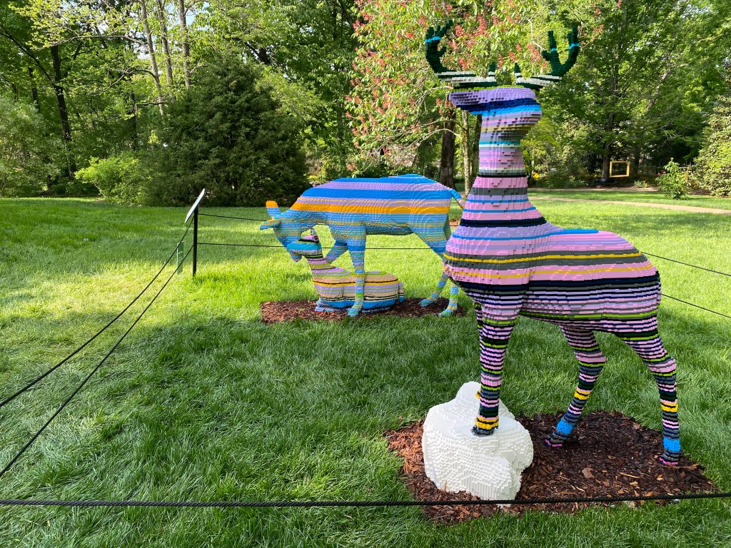 Lego buck and Lego doe and fawn with colorful horizontal stripes. Buck has blue, pink, purple, white, black, and yellow stripes. Doe and fawn have blue, light blue, orange, and purple stripes